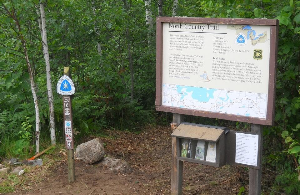Bulletin board at a trailhead in a forest that features a map and brochures.